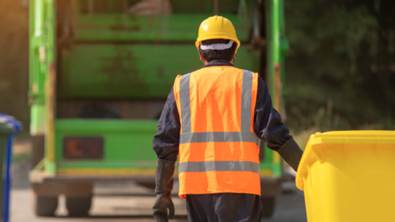 A person bringing a yellow garbage bin towards a garbage truck.