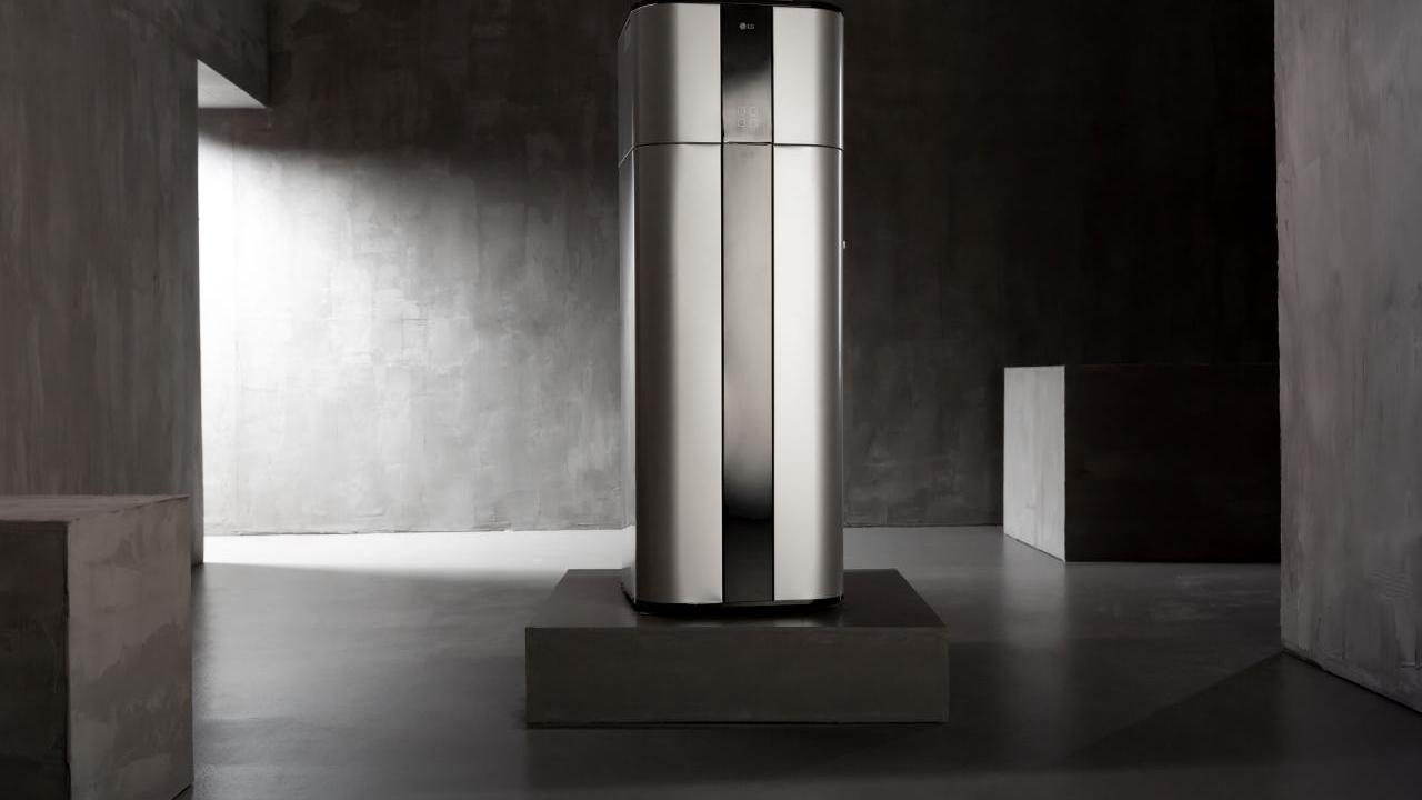 A sleek sliver and black heat pump machine on a grey square pedestal  in a stark smooth grey concrete room.