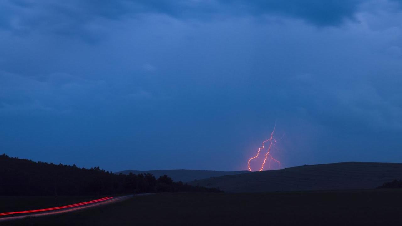 A cloudy sky with red lightning behind a distant hill