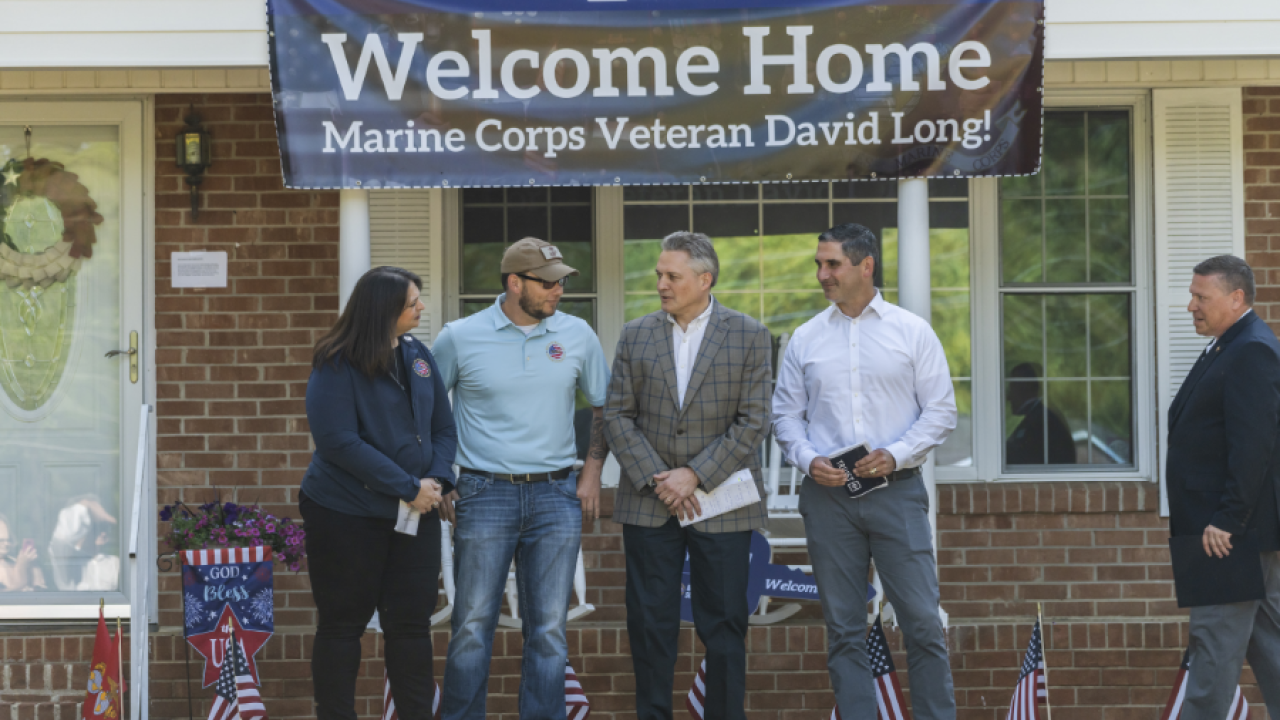 Sgt. David Long and three others stand outside his new home, a banner above them "Welcome Home"