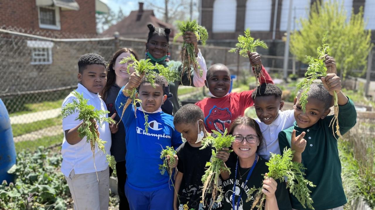 Kids and an adult holding up greens