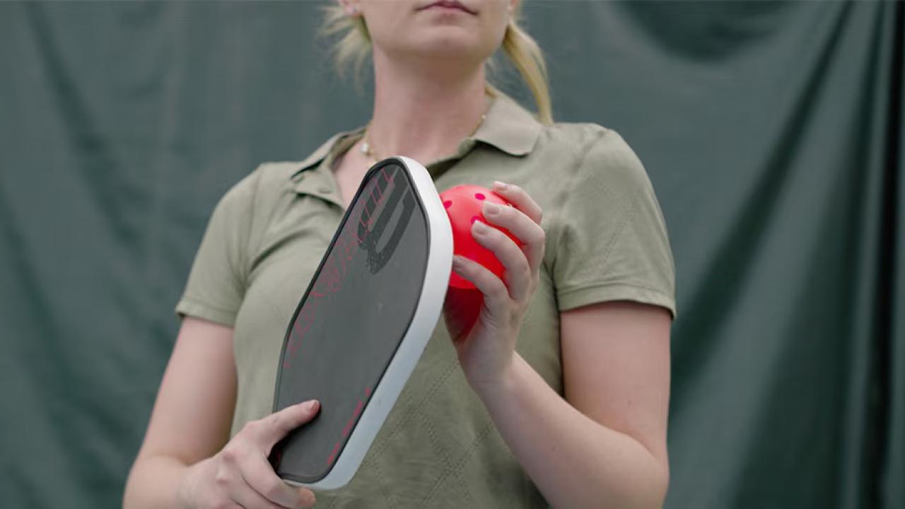 A person holding a pickleball racket and ball