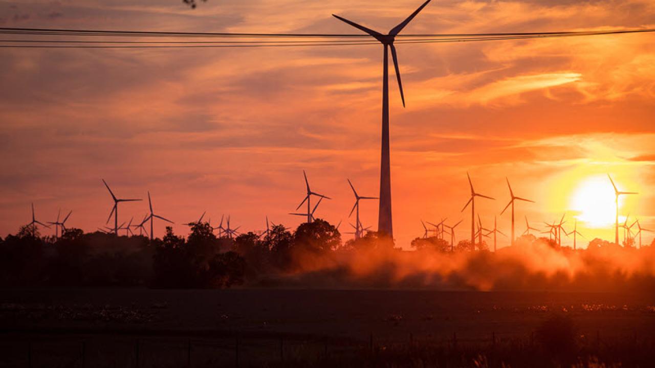 A sunsetting behind a large area with many wind turbines.