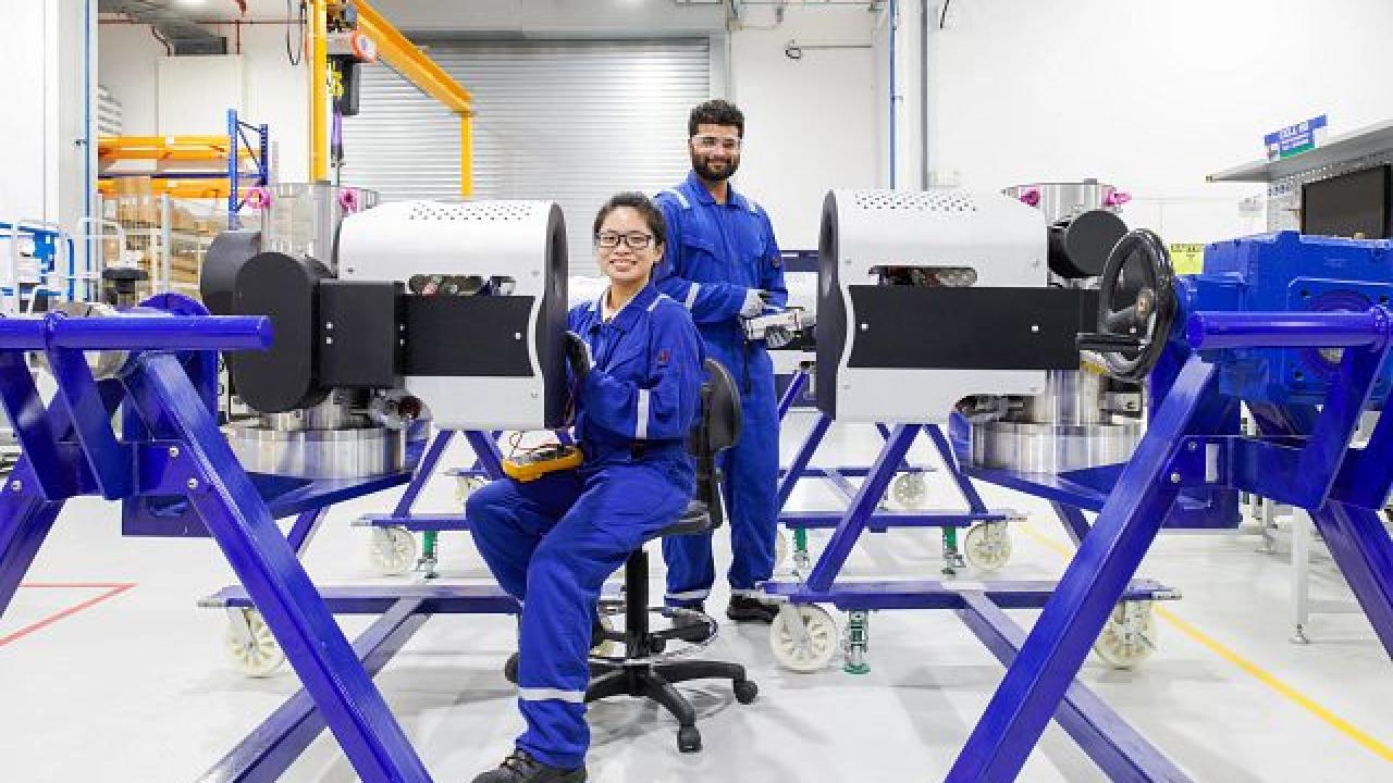 Two employees smiling at the camera. Each working on a piece of equipment