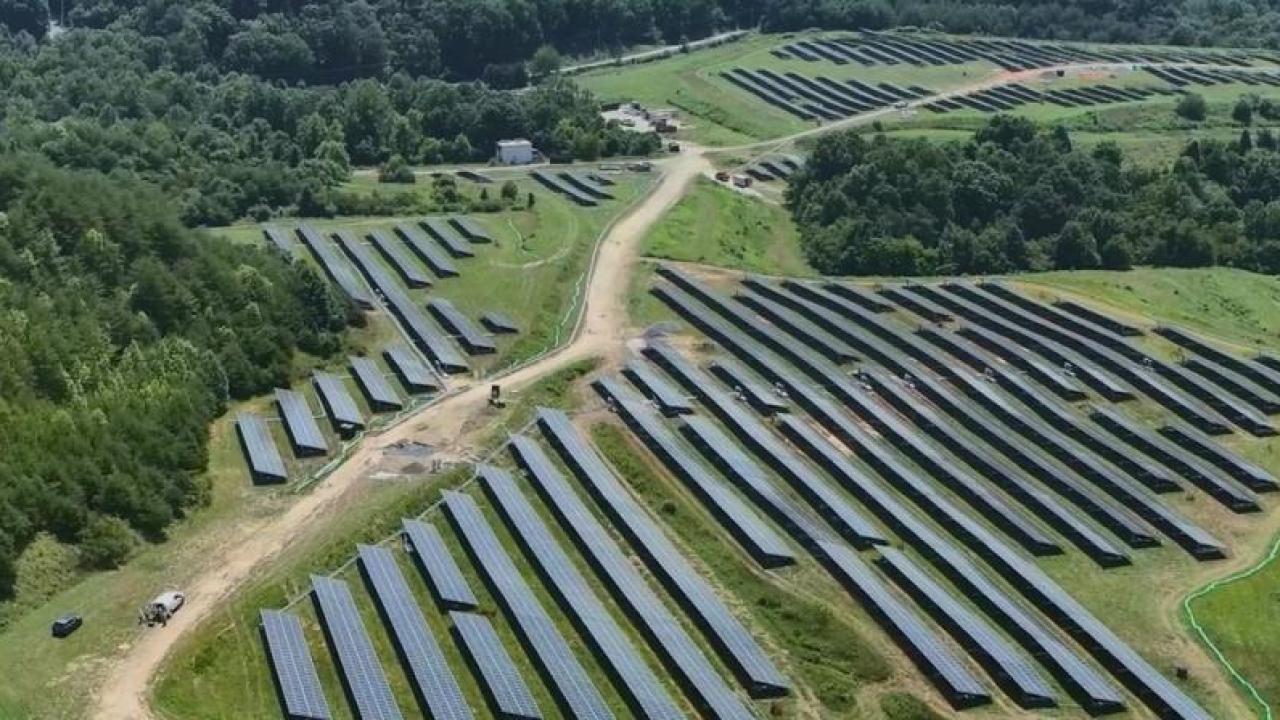 Aerial view of fields of rows of solar panels in a forested area.