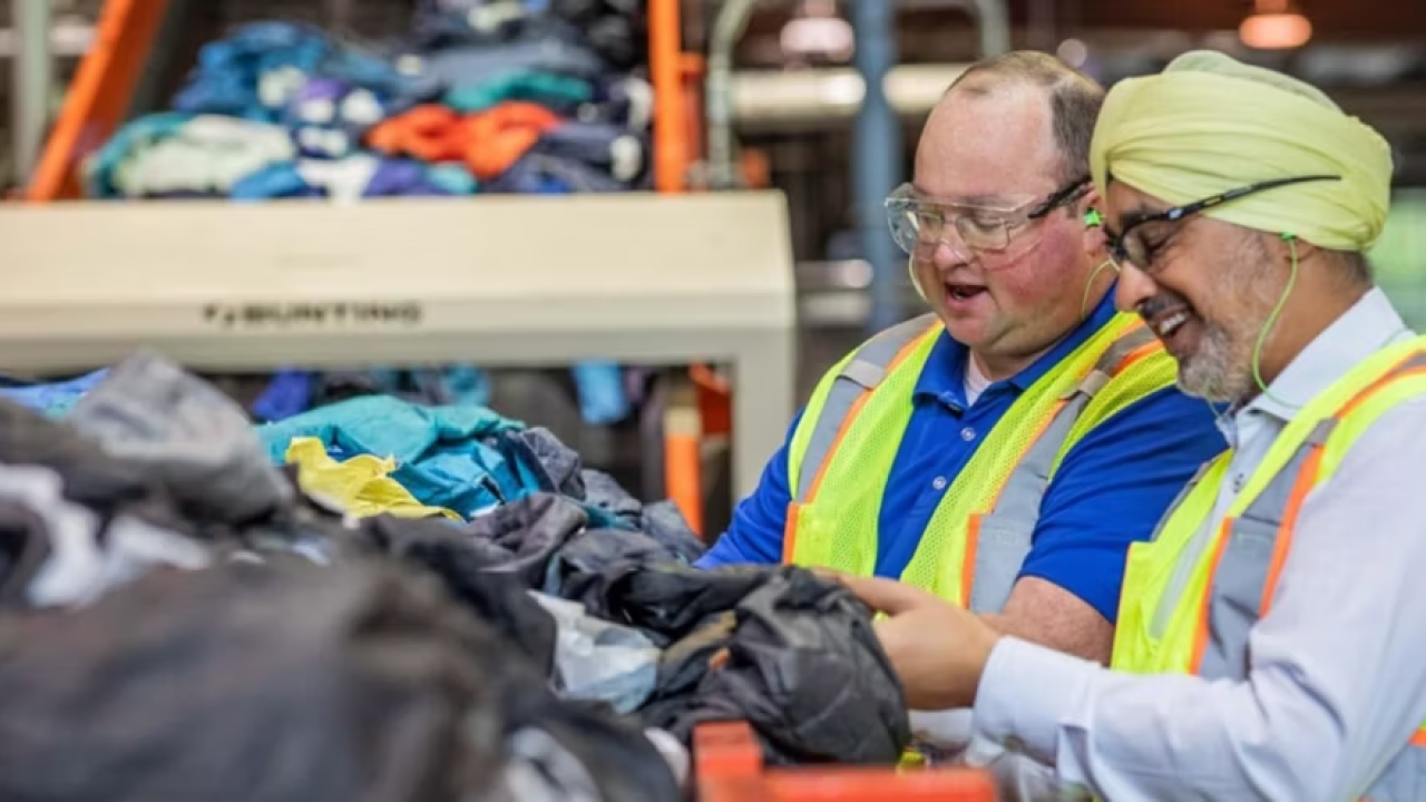 Two people in protective gear sort discarded textiles for recycling.