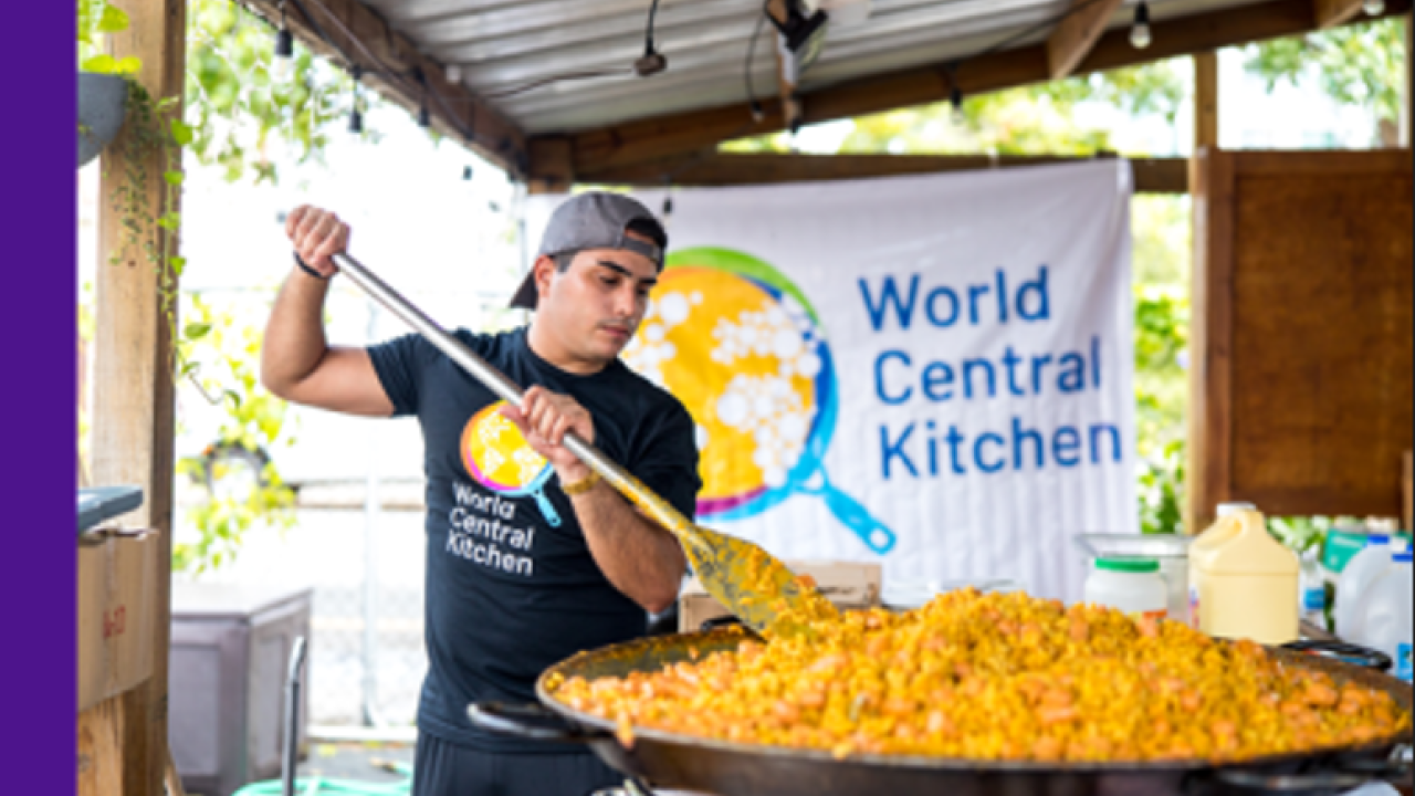 Volunteer cooking a big pot of food with a World Central Kitchen sign behind him 