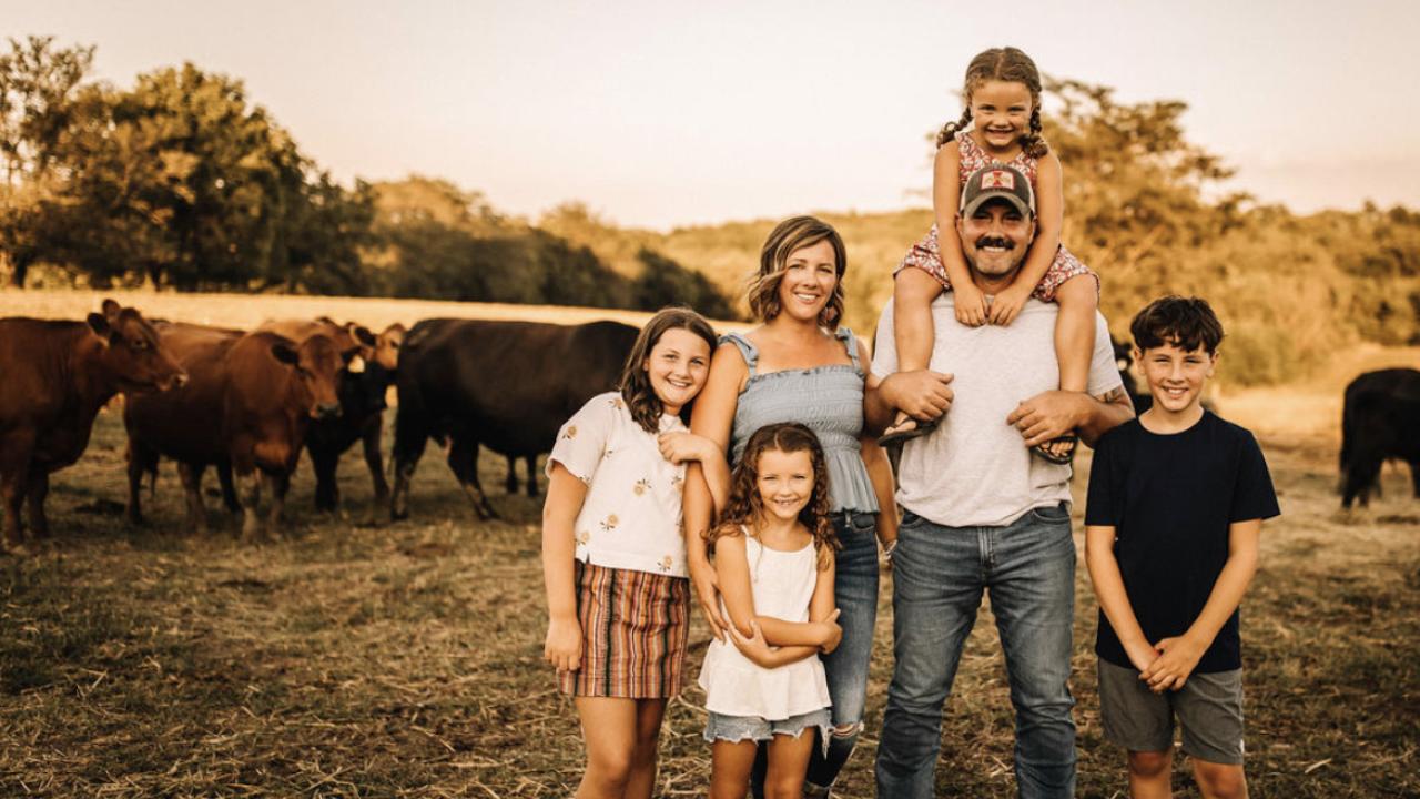 A family posed standing in a field in front of cows.