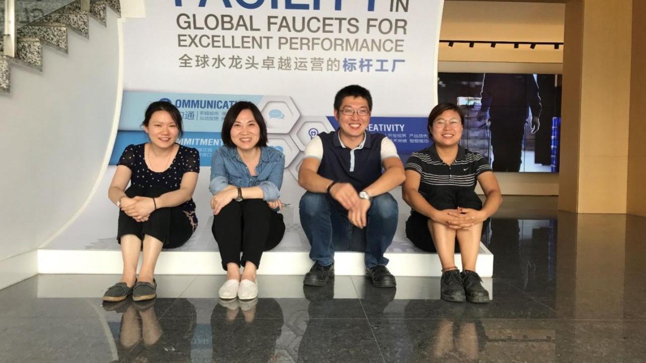 Four people seated in front of a sign "Benchmark facility in global faucets for excellent performance."
