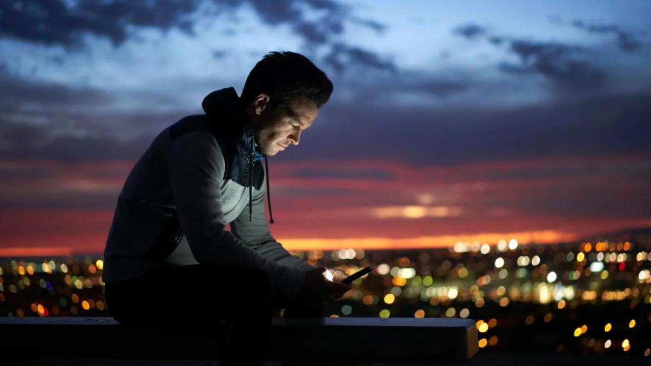A person looking at a device in the dark. A city scape behind them.