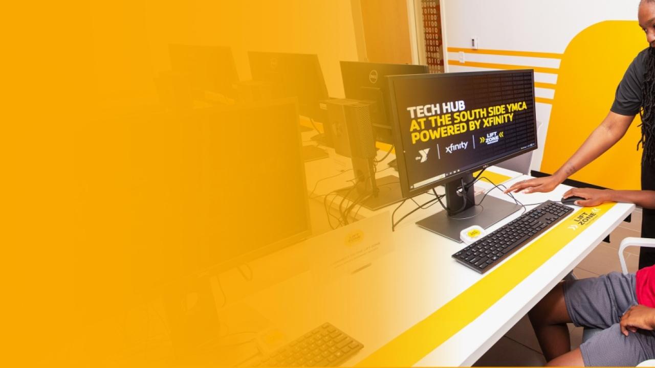 a staff member standing over a student working on a Tech Hub computer