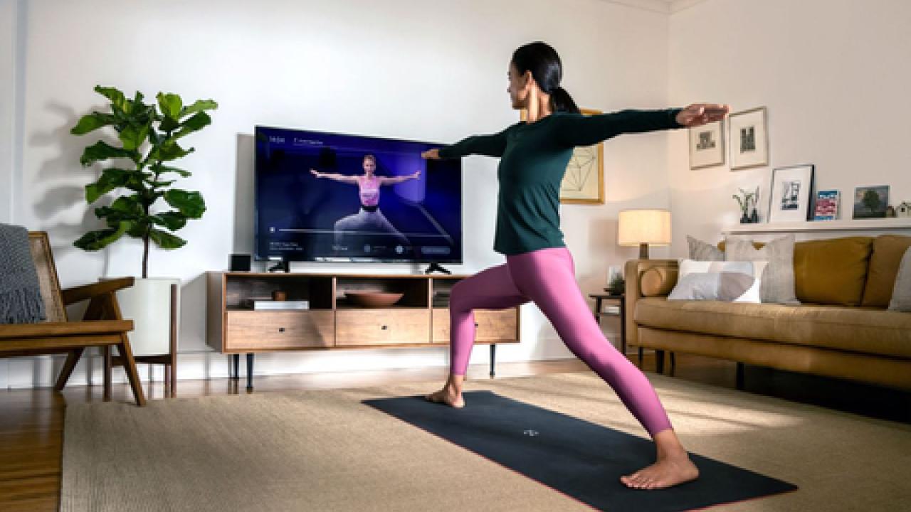 a person doing a yoga pose on a mat in a living room, watching an instructor on a tv screen