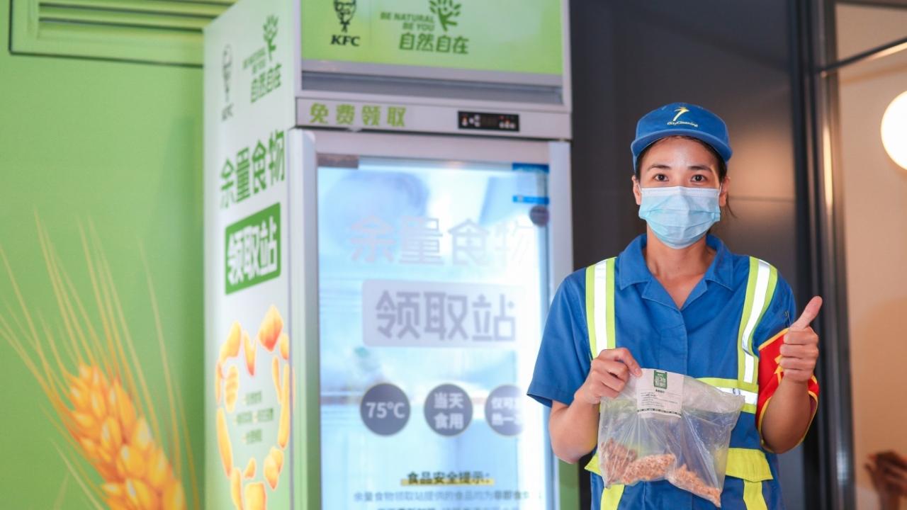 worker stands with a bag of food in front of a food bank refridgerator