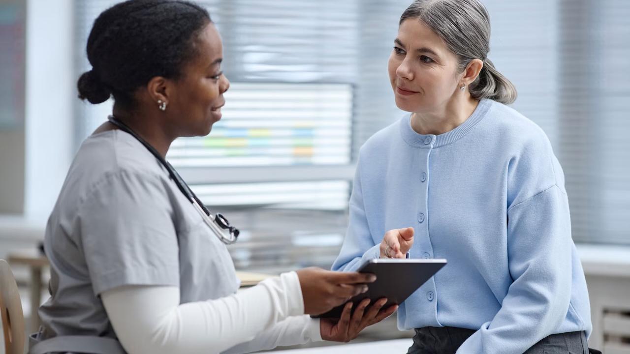 A patient and a health professional are sharing a tablet during a consultation.
