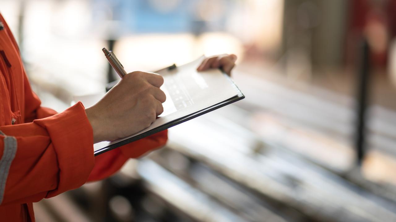 Worker in safety orange writing on a tablet