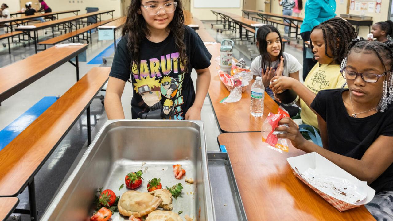 A student pushes a cart to collect food waste from fellow students in a school cafeteria.