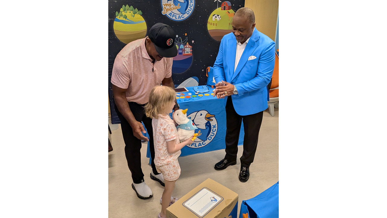 Former professional baseball and football player Brian Jordan (l) and Aflac Incorporated and Aflac U.S. President Virgil Miller (r) hand a My Special Aflac Duck to Leighton, a six year old patient at SSM Health Cardinal Glennon Children's Hospital in St. Louis.