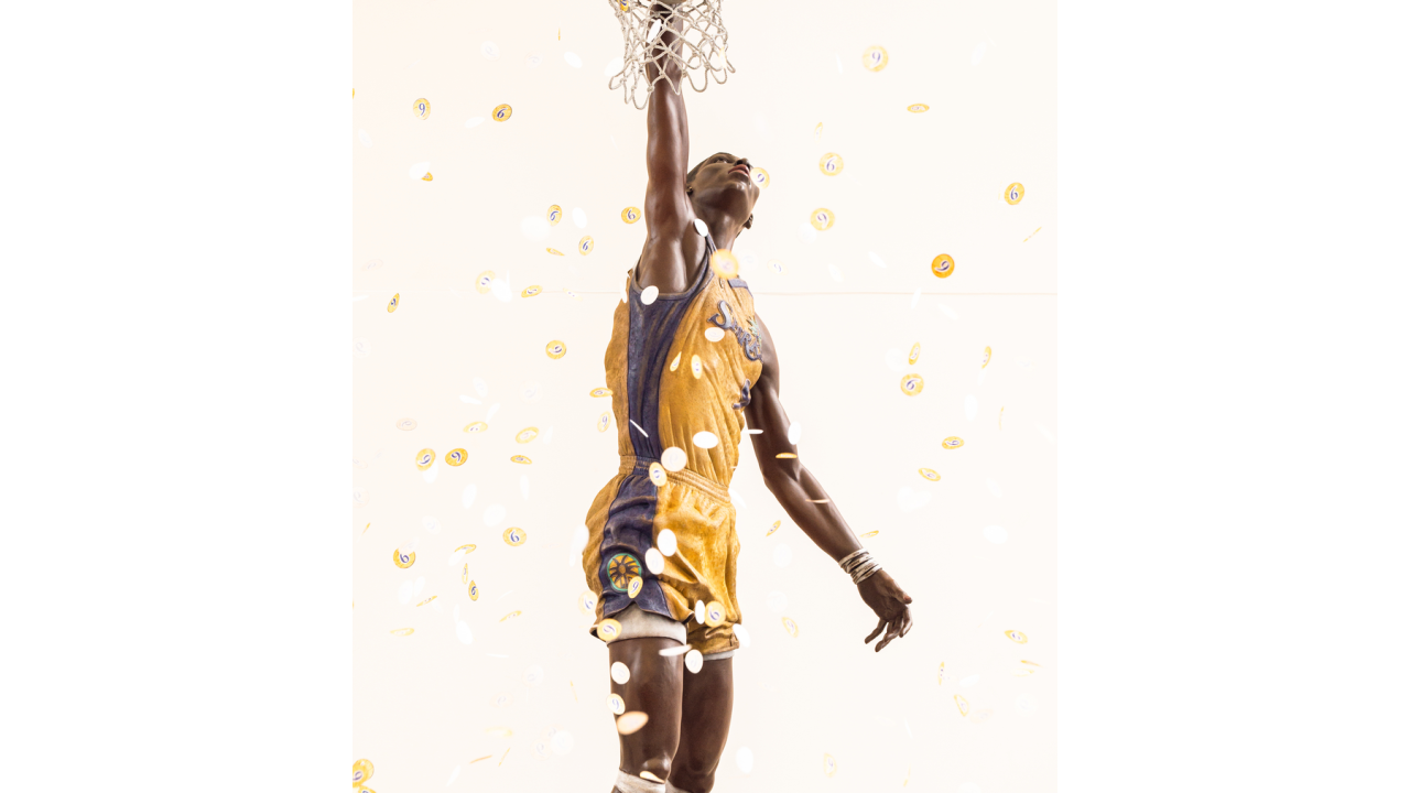 Close-up view of bronze Los Angeles Sparks basketball player Lisa Leslie statue reaching through the hoop as gold confetti falls around it.