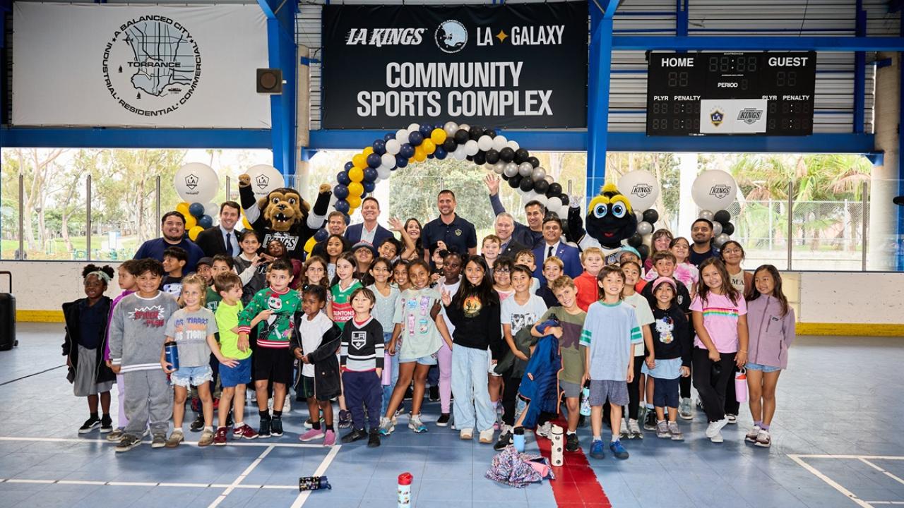 A large group of children and adults pose with the LA Kings and LA Galaxy mascots beneath signage for the LA Kings and LA Galaxy community sports complex in Torrance.