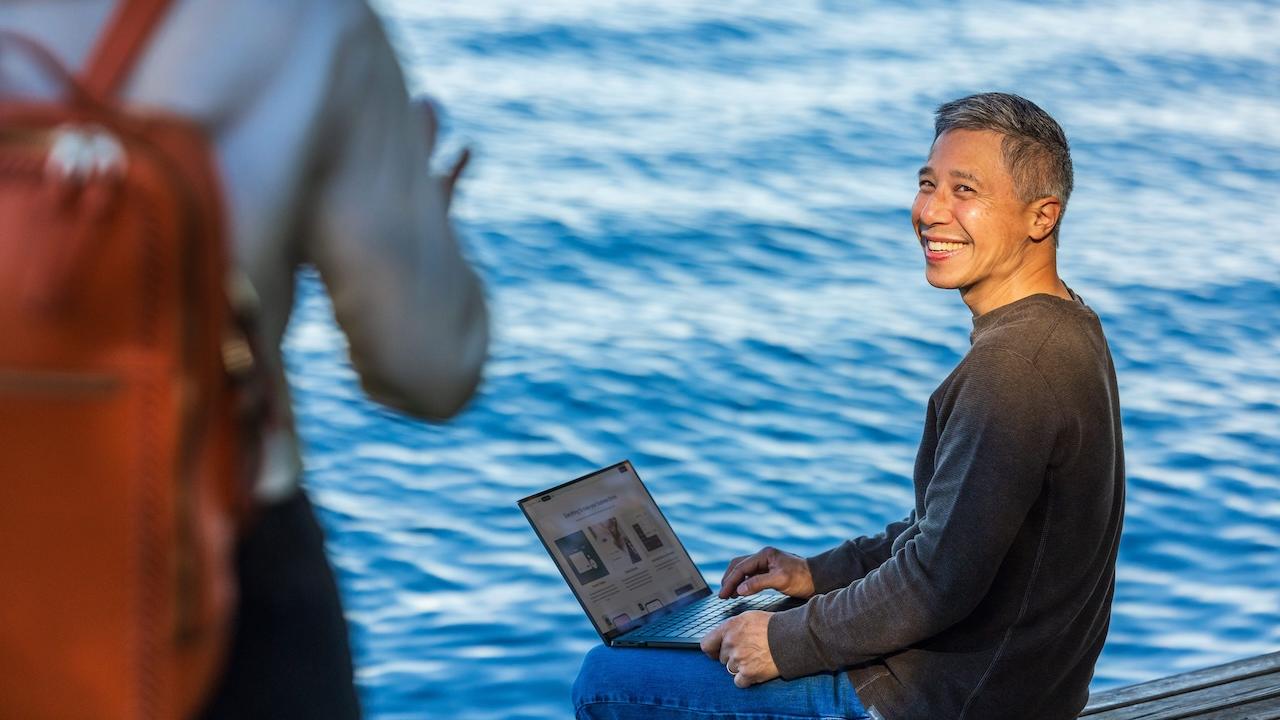 Person on a laptop seated next to a lake.