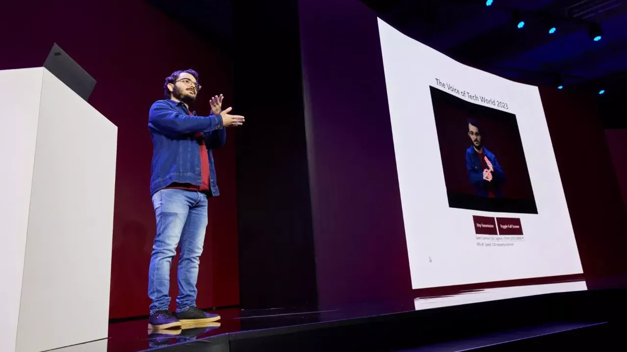 Gabriel presenting on stage using sign language and a digital display.
